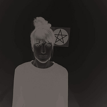 a person stands beside a pentagram. the colors have been reversed and it looks spooky
