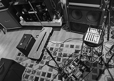 a theremin surrounded by sound equipement such as a mixer, effects pedals and speakers