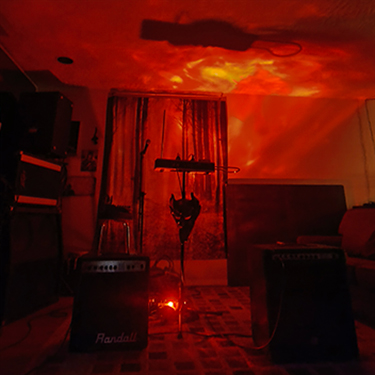 a red room with a theremin in the middle, and a mask hanging from the instrument stand