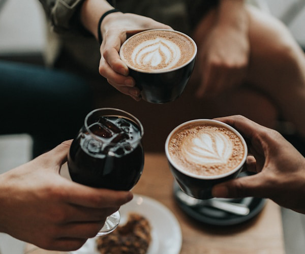 A trio of people enjoying hot and cold coffee drinks at a cafe