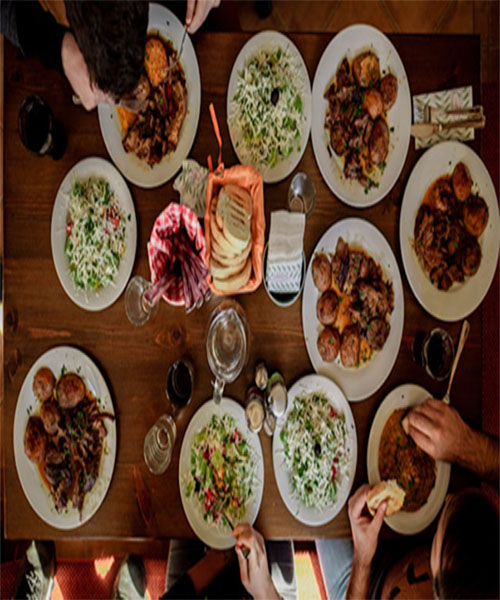 A picture of a table with multiple dishes and people eating from them.
